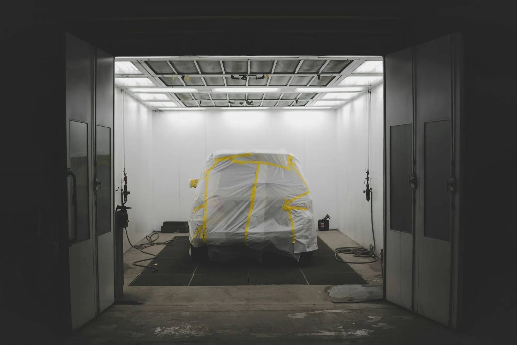 Car wrapped in masking film inside an empty, brightly lit paint booth