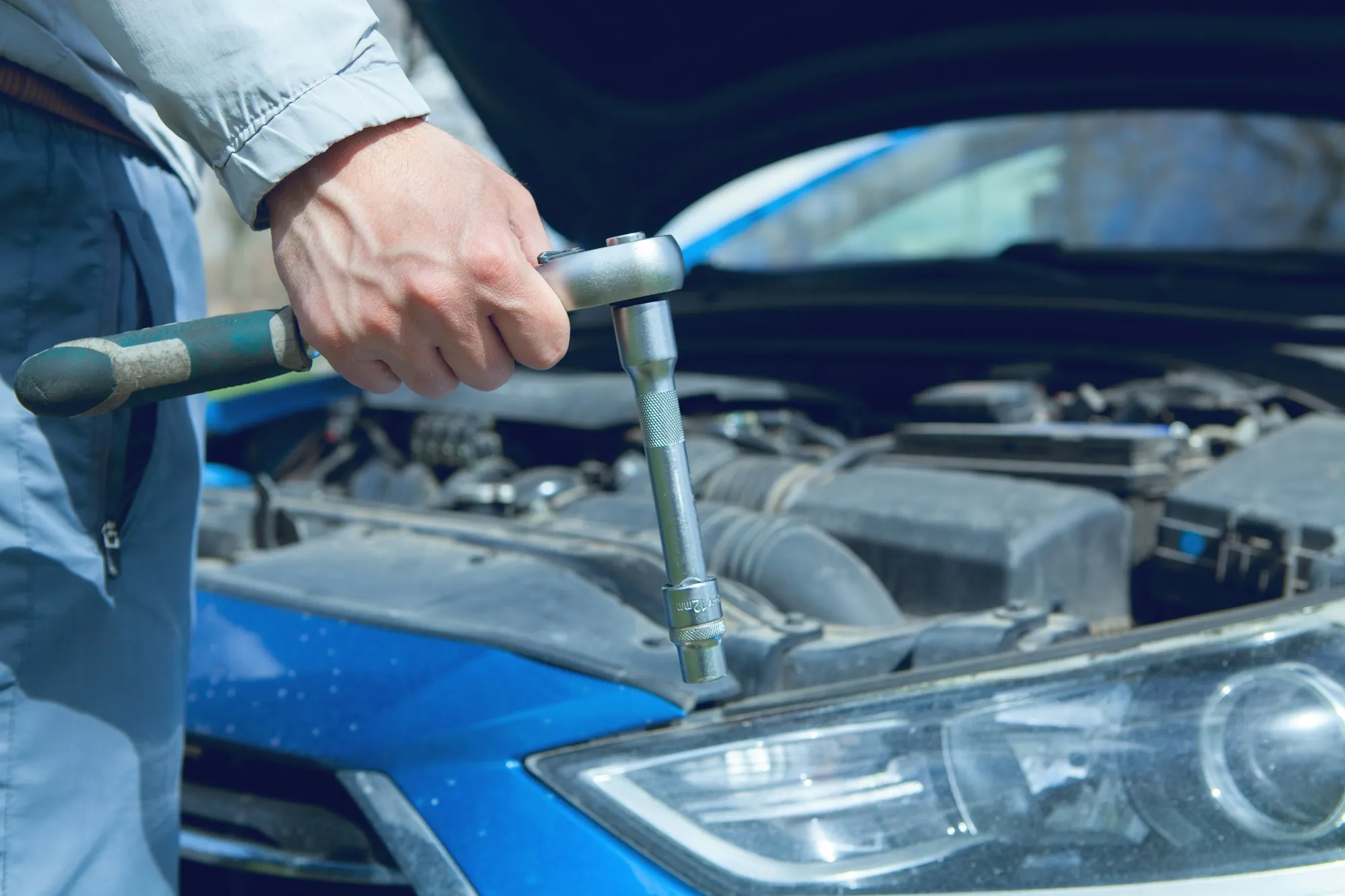 Mechanic turning a ratchet wrench in the engine bay of a blue car